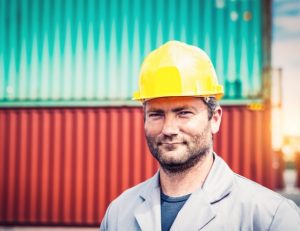 Man stands in front of steel shipping container, wearing a hard hat.